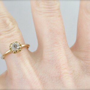 Puede incluir: Un anillo de compromiso de oro con un solo diamante redondo engastado en un delicado dise&ntilde;o floral.