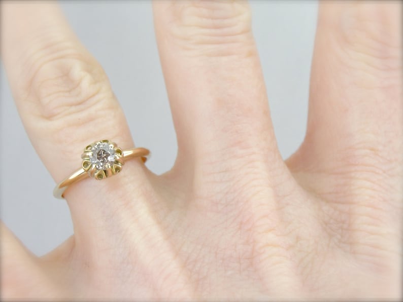 Puede incluir: Un anillo de compromiso de oro con un solo diamante redondo engastado en un delicado dise&ntilde;o floral.