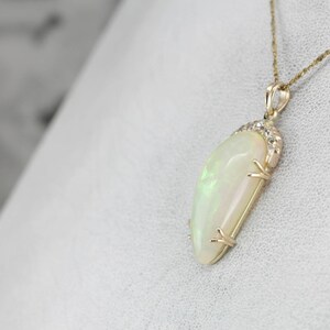 May include: A gold pendant necklace with a large, white opal gemstone. The opal is set in a gold setting with small diamonds around the edge.