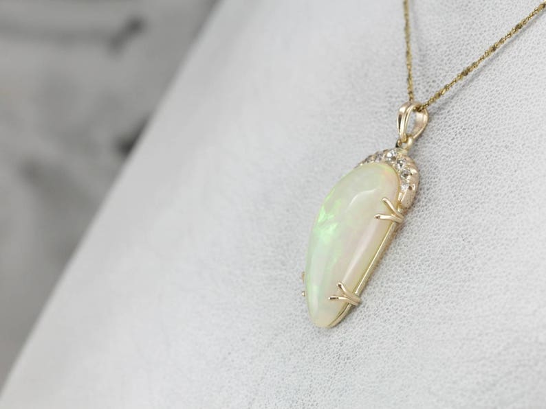 May include: A gold pendant necklace with a large, white opal gemstone. The opal is set in a gold setting with small diamonds around the edge.