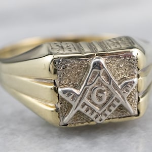 Może przedstawiać: Złoty pierścionek z kwadratowym wzorem przedstawiającym symbol masoński z literą 'G' w środku.