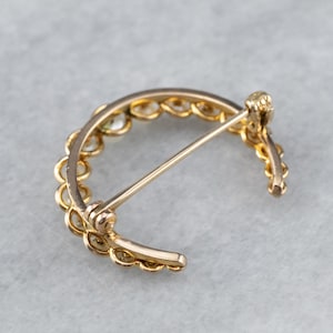 Puede incluir: Un broche de media luna de oro con una fila de peque&ntilde;as piedras redondas engastadas en el metal. El broche tiene un pasador y un cierre.
