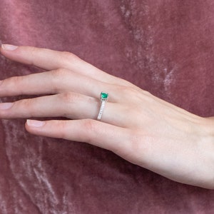 May include: A silver ring featuring a green emerald gemstone and a band of small diamonds.