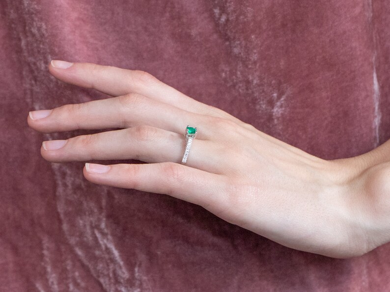May include: A silver ring featuring a green emerald gemstone and a band of small diamonds.