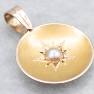May include: Gold-tone pendant featuring a central pearl and a starburst design. The pendant has a circular shape with a loop for a chain. The pearl is surrounded by a detailed star, adding elegance to the jewelry.