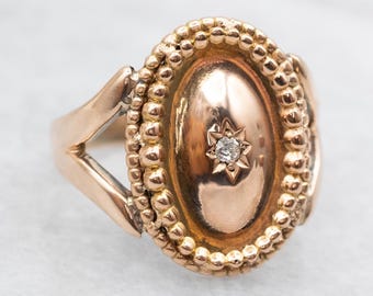 May include: A gold ring with a bezel set diamond in the center. The ring has a beaded edge and a V-shaped band.