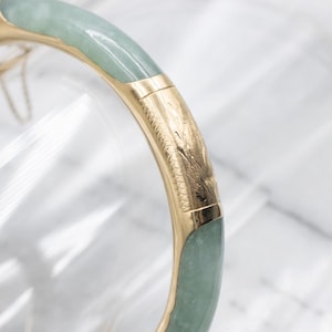 Può includere: Un braccialetto a cerchio con cerniera in oro con accenti di giadeite. Il braccialetto presenta una pietra di giada verde chiaro e un design inciso dettagliato sulla fascia d'oro. Un classico gioiello.