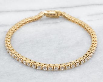 May include: A gold tennis bracelet with a row of small, clear diamonds.