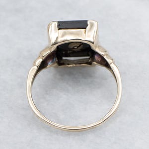 May include: A gold ring featuring a large, rectangular black gemstone. The ring has a classic design with decorative elements on the shoulders and a smooth, polished band. The gemstone is set in a secure bezel setting.
