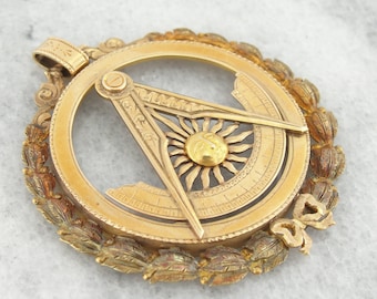 May include: A gold-toned pendant featuring a compass with a sunburst design and a compass rose. The pendant is surrounded by a wreath of leaves.