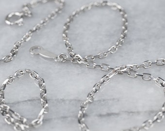 May include: Close-up of a silver chain necklace with an oval link design. The necklace is displayed on a light-colored surface, with the clasp and a portion of the chain visible. The chain is made of a shiny, metallic material.