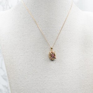 May include: A gold chain necklace with a small pendant featuring a pink and gold design.