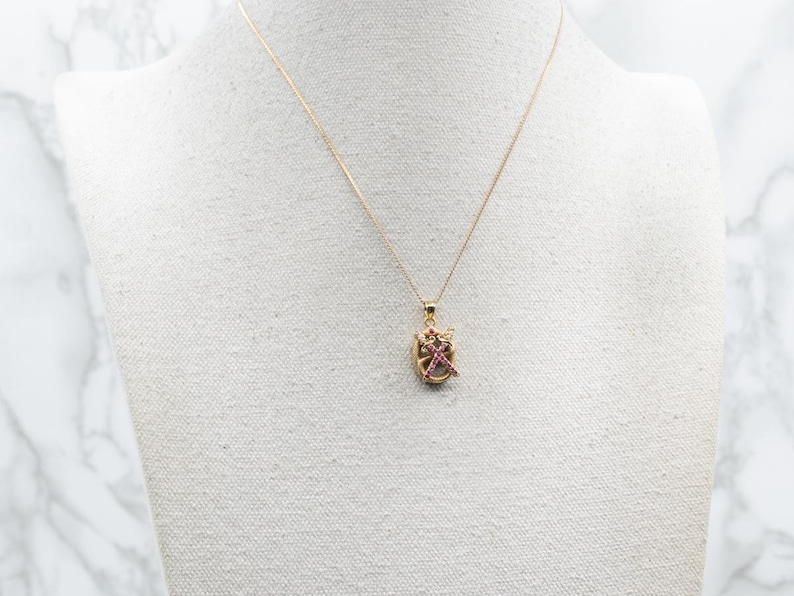 May include: A gold chain necklace with a small pendant featuring a pink and gold design.