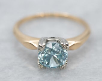 May include: A gold and silver ring with a light blue gemstone set in a prong setting.