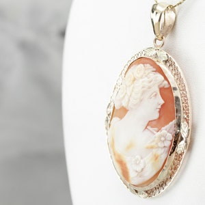 May include: A gold pendant featuring a cameo of a woman's profile carved from shell. The cameo is set in a delicate gold frame with a detailed design.