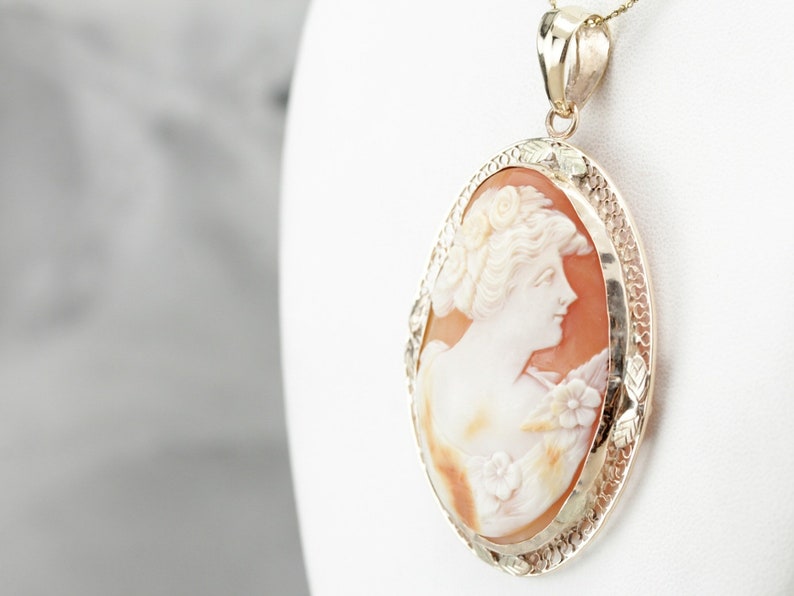 May include: A gold pendant featuring a cameo of a woman's profile carved from shell. The cameo is set in a delicate gold frame with a detailed design.