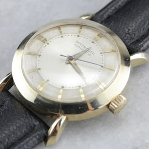 Pu&ograve; includere: Un orologio da polso Wittnauer Automatic color oro con quadrante bianco e cinturino in pelle nera.