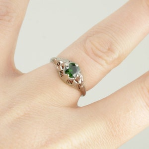 May include: A silver ring with a green gemstone set in a delicate filigree design.