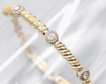 May include: Gold-toned bangle bracelet with a twisted rope design. The bracelet features three circular accents with a diamond-like stone in the center. The bracelet is displayed on a light background.