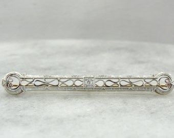 May include: A delicate silver and gold filigree brooch with a single diamond in the center.