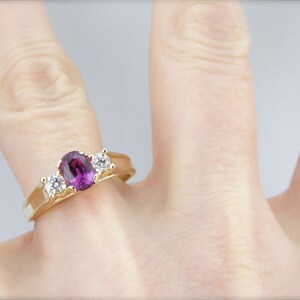 May include: A gold ring with a large oval purple gemstone and two smaller round white gemstones.