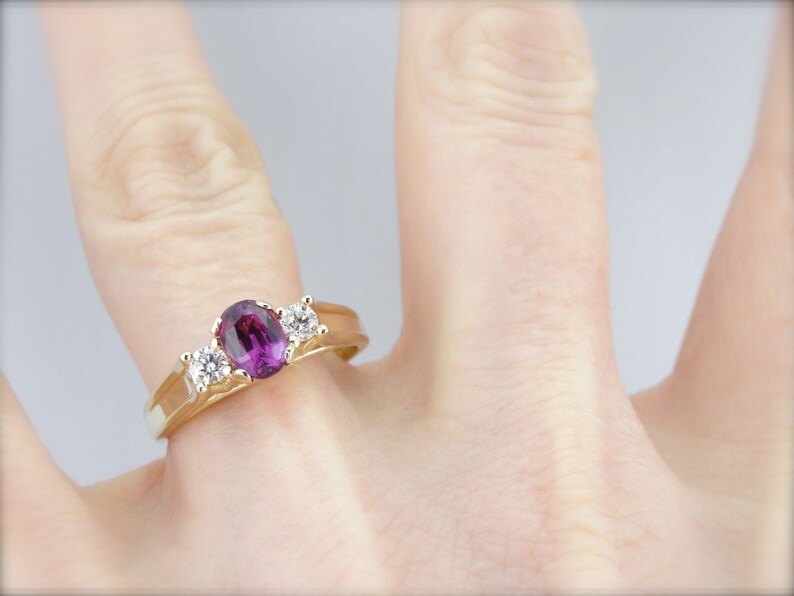 May include: A gold ring with a large oval purple gemstone and two smaller round white gemstones.