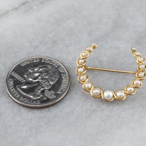 Puede incluir: Un broche de oro en forma de media luna con perlas blancas falsas. El broche es aproximadamente del tama&ntilde;o de una moneda de euro.