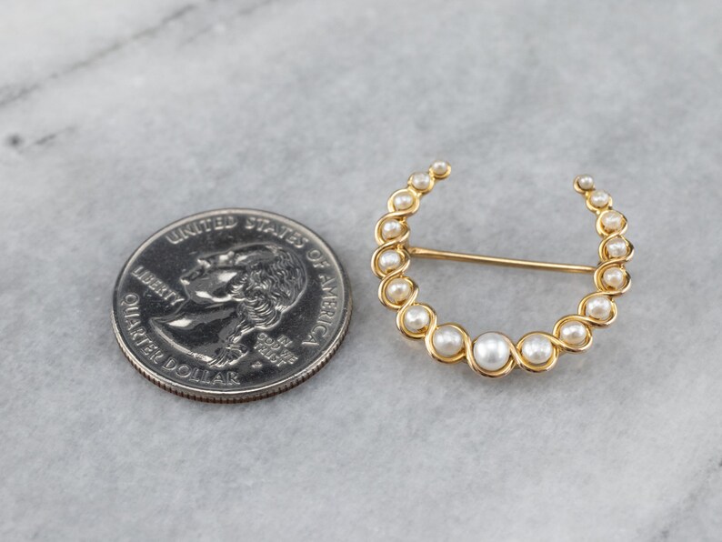 Puede incluir: Un broche de oro en forma de media luna con perlas blancas falsas. El broche es aproximadamente del tama&ntilde;o de una moneda de euro.