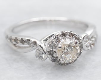 May include: A silver ring with a round diamond center stone surrounded by smaller diamonds. The band is twisted and features additional diamonds.