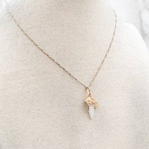 May include: A gold chain necklace with a white crystal pendant. The pendant is shaped like a pointed tooth with gold detailing.