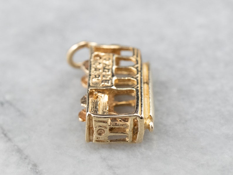 May include: Gold charm of a San Francisco cable car, a popular souvenir for visitors to the city.