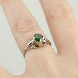 May include: A silver ring with a green gemstone set in a delicate filigree design.