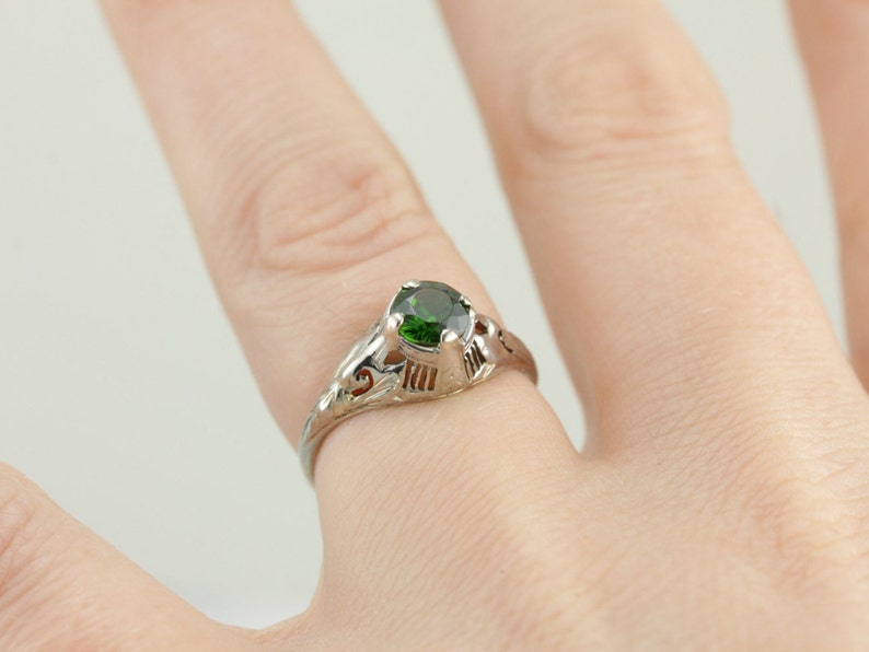 May include: A silver ring with a green gemstone set in a delicate filigree design.