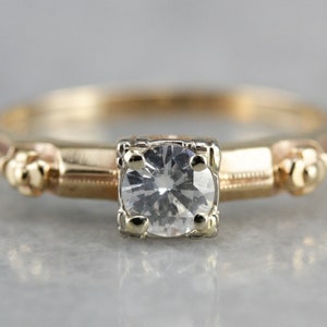 May include: A vintage gold engagement ring with a single round diamond set in a prong setting. The band features a delicate floral design.