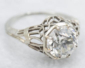 May include: A vintage engagement ring with a large, clear, round-cut diamond set in a delicate, filigree platinum setting.