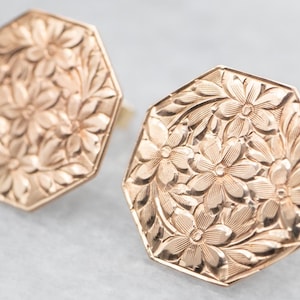 May include: A pair of gold-toned earrings featuring a floral design. The earrings are octagonal in shape and have a detailed, embossed pattern of flowers and leaves.