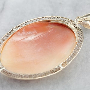 May include: A delicate silver filigree pendant featuring a large oval shell cameo. The cameo is a pale pink color with a smooth, polished surface.