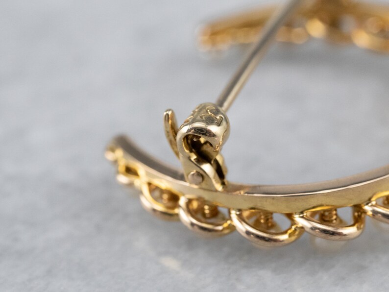 Puede incluir: Un broche de tono dorado en forma de media luna con un dise&ntilde;o detallado. El broche tiene un cierre de pin y enganche y est&aacute; marcado con la letra "K".