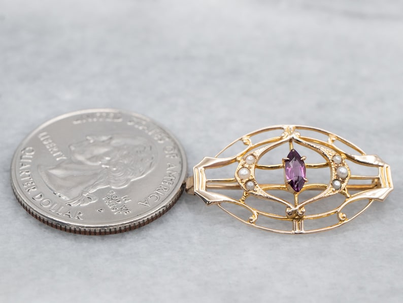 May include: A gold-toned brooch with a delicate, intricate design featuring a purple gemstone surrounded by small white pearls.