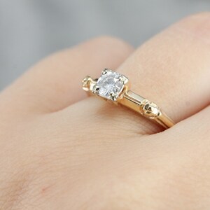 May include: A gold engagement ring with a single round diamond set in a prong setting. The band has a textured design.