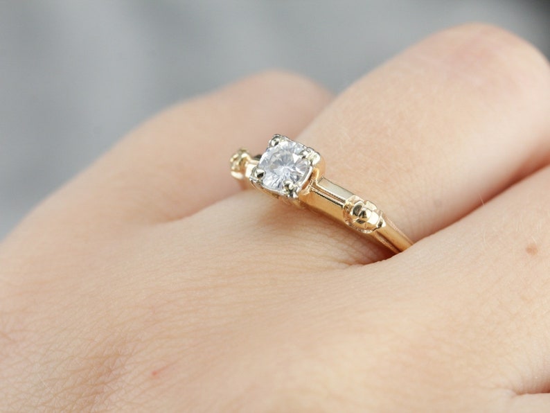 May include: A gold engagement ring with a single round diamond set in a prong setting. The band has a textured design.