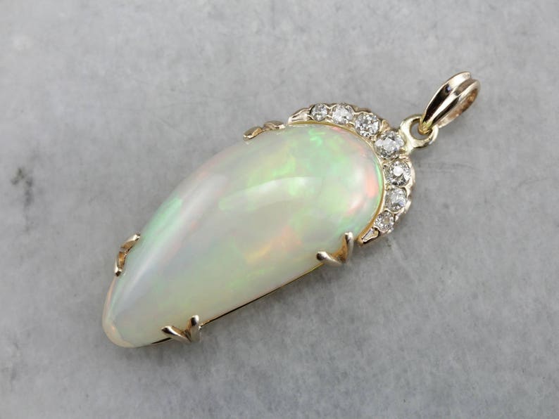 May include: A gold pendant featuring a large, white opal with a teardrop shape. The opal is surrounded by a halo of small, sparkling diamonds.