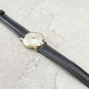 Pu&ograve; includere: Un orologio da polso dorato con quadrante bianco e cinturino in pelle nera. L'orologio ha un design classico ed &egrave; in buone condizioni.