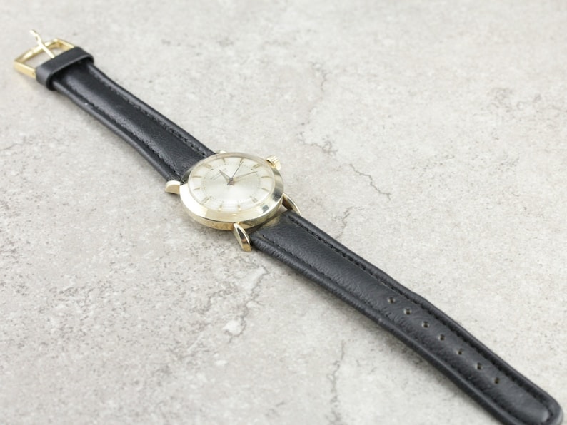 Pu&ograve; includere: Un orologio da polso dorato con quadrante bianco e cinturino in pelle nera. L'orologio ha un design classico ed &egrave; in buone condizioni.