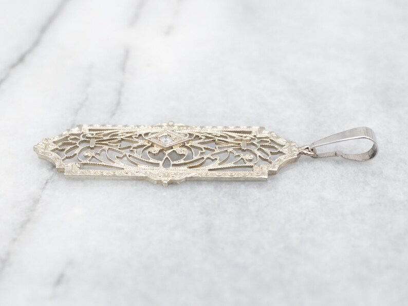 May include: A delicate gold pendant with a filigree design and a single diamond in the center.
