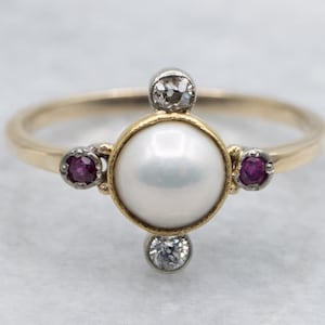 May include: A gold ring featuring a central white pearl, framed by a gold setting. The ring is accented with two small, round, deep red gemstones and two clear, sparkling diamonds. The band is a simple, polished gold.