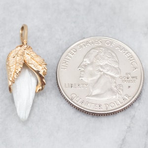 May include: A gold pendant featuring a white, pearlescent flower with two gold leaves. The pendant is shown next to a US quarter for size comparison.