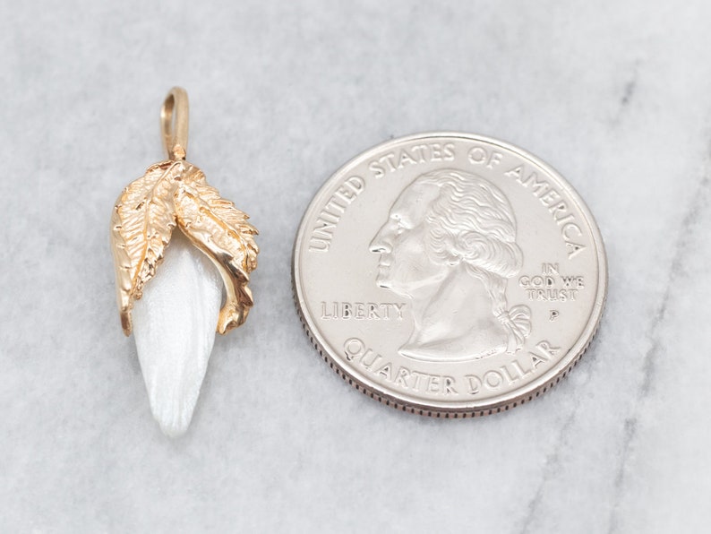 May include: A gold pendant featuring a white, pearlescent flower with two gold leaves. The pendant is shown next to a US quarter for size comparison.