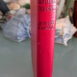 May include: A red hardcover book titled "Black Bartlemy's Treasure" by Jeffery Farnol. The title and author's name are in black lettering. The book's spine is visible, showcasing the title and author.