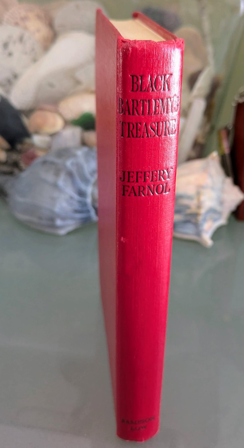 May include: A red hardcover book titled "Black Bartlemy's Treasure" by Jeffery Farnol. The title and author's name are in black lettering. The book's spine is visible, showcasing the title and author.
